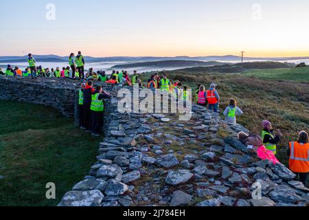 Menschenmengen beobachten den Sonnenaufgang nach der Dunkelheit in das Licht. Knockdrum Steinring Fort, West Cork, Irland Stockfoto