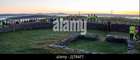 Menschenmengen beobachten den Sonnenaufgang nach der Dunkelheit in das Licht. Knockdrum Steinring Fort, West Cork, Irland Stockfoto