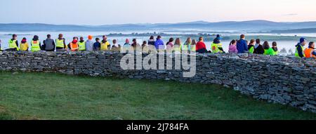 Menschenmengen beobachten den Sonnenaufgang nach der Dunkelheit in das Licht. Knockdrum Steinring Fort, West Cork, Irland Stockfoto