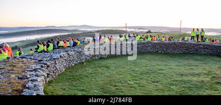 Menschenmengen beobachten den Sonnenaufgang nach der Dunkelheit in das Licht. Knockdrum Steinring Fort, West Cork, Irland Stockfoto