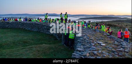 Menschenmengen beobachten den Sonnenaufgang nach der Dunkelheit in das Licht. Knockdrum Steinring Fort, West Cork, Irland Stockfoto