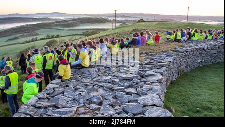 Menschenmengen beobachten den Sonnenaufgang nach der Dunkelheit in das Licht. Knockdrum Steinring Fort, West Cork, Irland Stockfoto