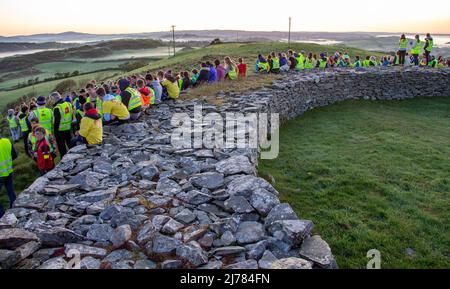 Menschenmengen beobachten den Sonnenaufgang nach der Dunkelheit in das Licht. Knockdrum Steinring Fort, West Cork, Irland Stockfoto