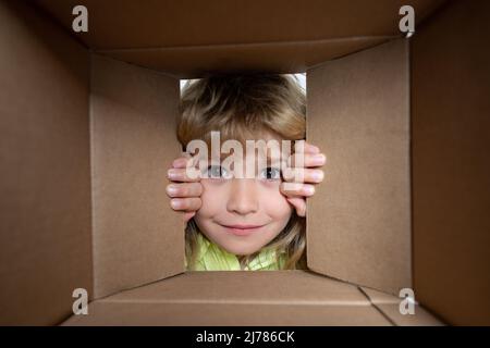 Kind öffnen Papier Karton-Box. Kind Junge Auspacken und Öffnen Karton-Box Blick nach innen mit Überraschung Gesicht. Pakete und Lieferung. Stockfoto