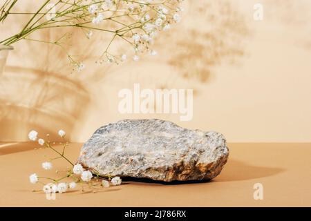 Steinständer auf einem beigefarbenen Tisch mit Gypsophila-Blüten im Sonnenlicht. Nachbau für Parfüm oder Kosmetik. Stockfoto