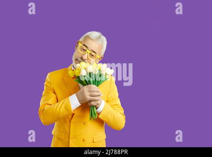 Nahaufnahme Porträt glücklich, Senior Mann, hält, riechende Bouquet von gelben Tulpen in der Hand, isoliert lila Hintergrund. Menschliche Emotionen, Gesichts- und Gesichtszüge Stockfoto