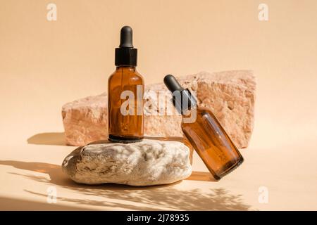 Dunkle, bernsteinfarbene Glasflasche, die auf Stein steht. Natürliche Hautpflege SPA Beauty-Produkt-Design. Mineralische Bio-Öl-Kosmetik auf beigem Hintergrund. Stockfoto