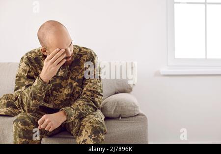 Deprimierter Veteran, der nach einer traumatischen Belastungsstörung auf dem Sofa zu Hause sitzt Stockfoto