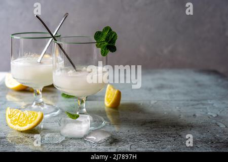 Zitronensorbet in zwei Gläsern mit Zitronen, Eiswürfeln, Teelöffeln, Minzblättern auf grauem Hintergrund mit Kopierfläche Stockfoto