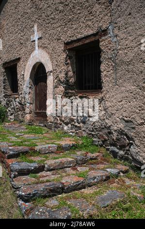 Orangefarbene Flechten stellen alte Stufen auf, die zur rustikalen Dorfkirche Sant Pere del Serrat aus dem frühen 16.. Jahrhundert in El Serrat im Ordino-Tal, Andorra, führen. Der rechteckige Innenraum verfügt über eine Holzgalerie und ein Ende 1500s oder Anfang 1600s bemaltes Altarbild, das dem heiligen Petrus gewidmet ist. Stockfoto