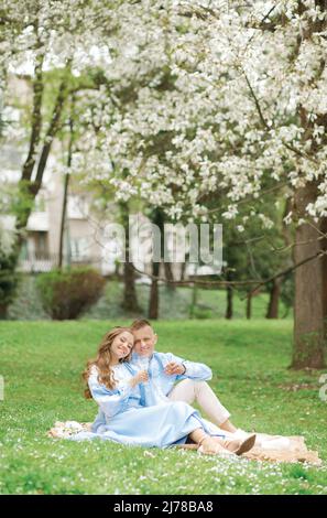 Liebevolles Paar, das im Frühling im Park sitzt, mit einem Glas Champagner in den Händen Stockfoto