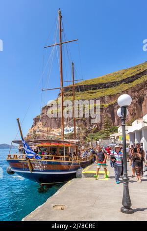 Fira, Santorini, Griechenland - 26. April 2019: Menschen am alten Hafen und Ausflugsboot Stockfoto