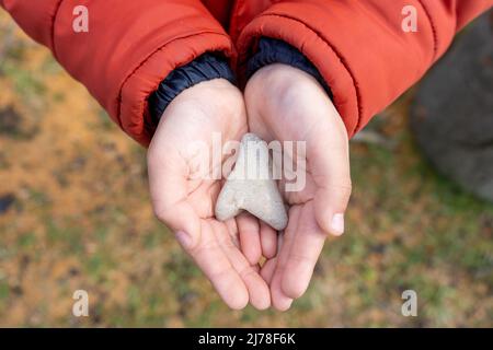 Die Hände des Kindes halten einen herzförmigen Stein aus der Nähe Stockfoto