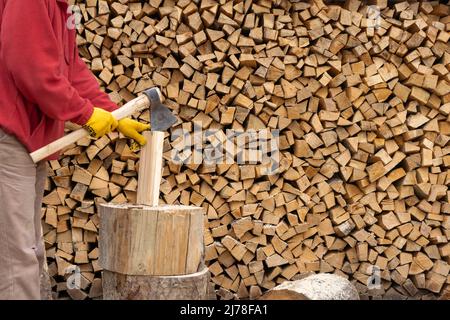 Junger Mann hackt Feuerholz und Axt Stockfoto