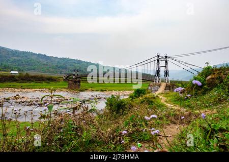 Isolierte Eisen Hängebrücke über fließenden Fluss mit nebligen Berg Hintergrund am Morgen Bild wird bei Nongjrong meghalaya indien aufgenommen. Stockfoto