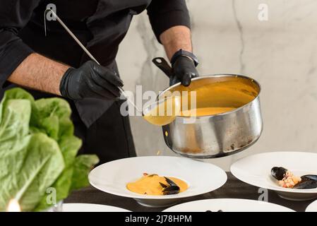 Der Küchenchef bereitet in einem Restaurant Karotten-Sahnesuppe mit Meeresfrüchten zu Stockfoto