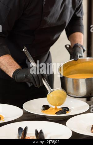 Der Küchenchef bereitet in einem Restaurant Karotten-Sahnesuppe mit Meeresfrüchten zu Stockfoto