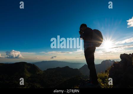 Der Fotograf, der auf einem Bergvorsprung steht und den wunderschönen Sonnenuntergang vor einer blauen Himmelswolke genießt, Doi Chiang Daw, Thailand Stockfoto