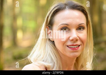 Nahaufnahme Porträt einer schönen lächelnden blonden Frau mit hellbraunen Augen im Wald Stockfoto