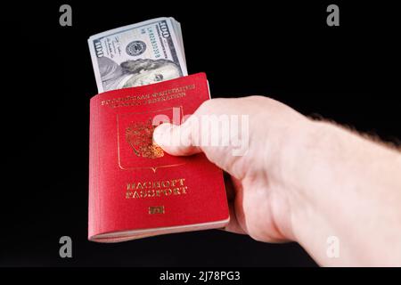 kaukasische Hand mit russischem internationalem Pass und US-Papierdollar auf schwarzem Hintergrund Stockfoto