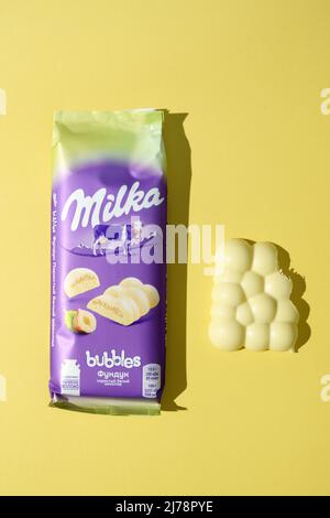 Tjumen, Russland-03. März 2022: Weiße Milchschokolade mit Haselnüssen milka. Gelber Hintergrund. Beliebte Schokolade Stockfoto