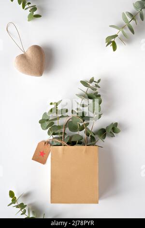 Basteltasche mit Eukalyptus im Winter und weißer Helleborus-Blume. Brauner Papieranhänger. Stockfoto