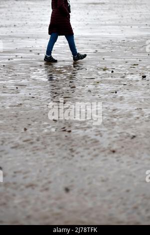 Alleinstehende weibliche Figur, die bei Ebbe am nassen Sandstrand entlang im Norden norfolk englands läuft Stockfoto