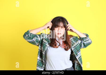 Die mollige asiatische Frau, die auf dem gelben Hintergrund mit der lässigen Kleidung steht. Stockfoto