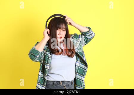 Die mollige asiatische Frau, die auf dem gelben Hintergrund mit der lässigen Kleidung steht. Stockfoto