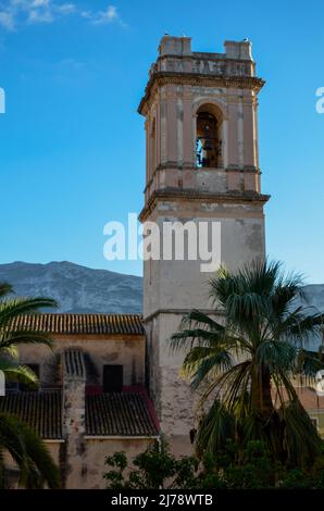 Der Glockenturm der alten Kirche Església de l'Assumpció de Dénia hinter einigen Palmen in der Innenstadt von Denia Stockfoto