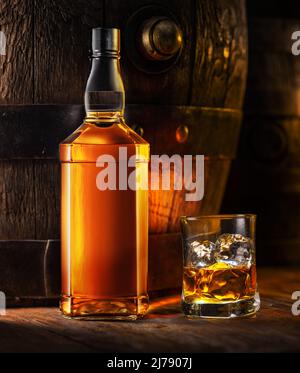 Whisky-Flasche und ein Glas Whisky. Altes Holzfass im Hintergrund. Stockfoto