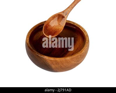 Sonnenblumenöl fließt von einem Holzlöffel in eine Holzschale. Kopierbereich, weißer Hintergrund. Stockfoto