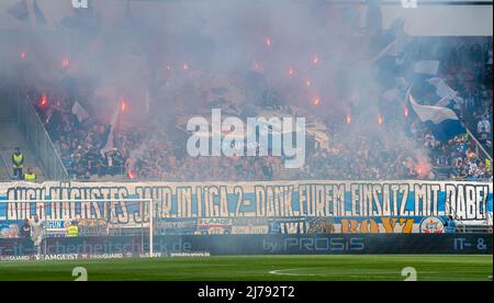 07. Mai 2022, Bayern, Ingolstadt: Fußball: 2. Bundesliga, FC Ingolstadt 04 - Hansa Rostock, 33. Spieltag, Audi Sportpark. Rostocker Fans starten Pyrotechnik hinter Rostocker Torwart Markus Kolke. Foto: Stefan Puchner/dpa - WICHTIGER HINWEIS: Gemäß den Anforderungen der DFL Deutsche Fußball Liga und des DFB Deutscher Fußball-Bund ist es untersagt, im Stadion und/oder des Spiels aufgenommene Fotos in Form von Sequenzbildern und/oder videoähnlichen Fotoserien zu verwenden oder zu verwenden. Stockfoto