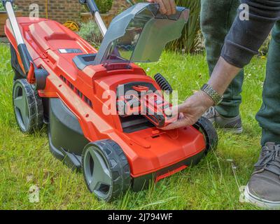 Gärtner beim Wechseln der Lithium-Ionen-Batterie eines elektrischen kabellosen Rasenmähers Stockfoto