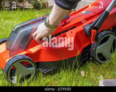 Gärtner für Männer, der die Schnitthöhe auf einem Akku-Rasenmäher mit Lithium-Ionen-Akku anpasst Stockfoto