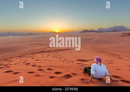 Frau, die den wunderschönen Sonnenuntergang in der Wadi Rum Wüste in Jordanien genießt, mit Blick auf die fernen Berge. Stockfoto