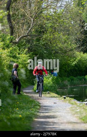 Frau in roter Jacke fährt mit dem Mountainbike auf einem Kanalpfad in der Sonne Stockfoto