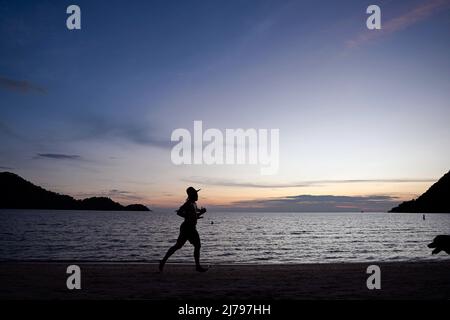 30. April 2022, Koh Chang, Thailand: Eine Silhouette eines Mannes, der mit seinem Hund am Strand entlang läuft, in der Blue Haven Bay von Siam Royal View am Chang Noi Beach, Koh Chang Island in der Provinz trat. Koh Chang ist eine beliebte Touristeninsel, die etwa 350 km südöstlich der Hauptstadt Bangkok liegt. (Bild: © Paul Lakatos/SOPA Images via ZUMA Press Wire) Stockfoto