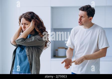 Die lockige Frau steckt sich die Ohren in Stress und will nicht hören, wie der verärgerte Ehemann zankt und über Familienprobleme aus der Nähe argumentiert Stockfoto