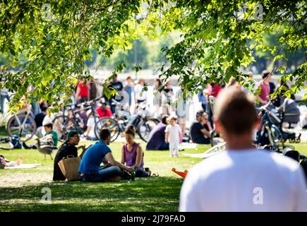 07. Mai 2022, Hessen, Frankfurt/Main: Zahlreiche Menschen haben sich in der Sonne auf dem Gras inmitten des frischen Grüns am Mainufer niedergelassen. Foto: Frank Rumpenhorst/dpa Stockfoto