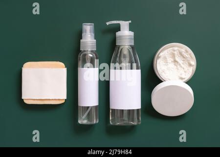 Hausgemachte Kosmetik in Plastikröhrchen und Flaschen auf dunkelgrüner Draufsicht. Modell der Markenverpackung. Bio-Naturkosmetik für die Haut- und Haarpflege Stockfoto