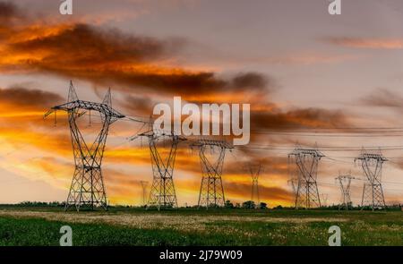 Hochspannungsleitungen, Hochspannungstürme für elektrische Hochspannungsübertragung am farbenprächtigen, wolkigen Himmel bei Sonnenuntergang, Kopierraum Stockfoto