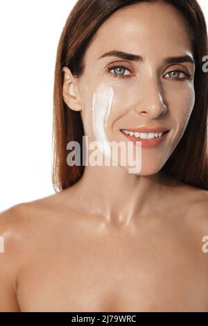 Vertikales Porträt einer Frau mittleren Alters, die Anti-Aging-Maske aufsetzt, die Haut mit Gesichtspeeling nährt, tägliche Pflegecreme, lächelnd, stehend Stockfoto