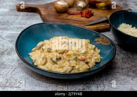 Risotto mit Pilzen und sonnengetrockneten Tomaten in einer blauen Schüssel Stockfoto