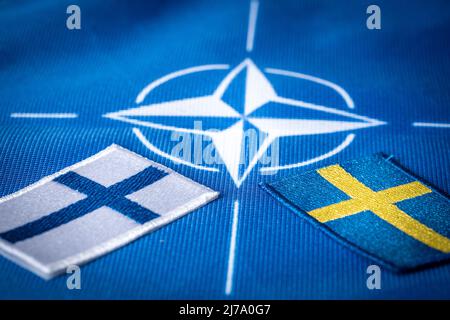 Flaggen Schwedens und Finnlands vor dem Hintergrund des NATO-Symbols, dem Konzept der skandinavischen Länder, die dem Nordatlantikbündnis beitreten Stockfoto