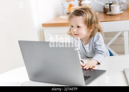 Kleine schöne Mädchen zu Hause studieren, während Quarantäne. Nettes Kind macht Hausaufgaben online sitzen in der Küche . Das Konzept des Lernens zu Hause für Stockfoto