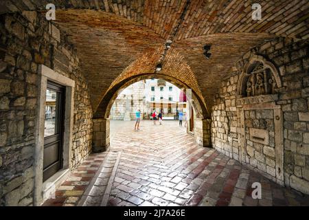 Das Quadrat der Arme öffnet sich vor wie Touristen die gated, ummauerten mittelalterlichen Festung Stadt Kotor, Montenegro geben Sie über den Tunnel Eingang Stockfoto