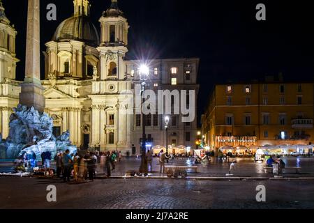 Nächtlicher Blick auf die Piazza Navona mit beleuchteten Cafés, die Kirche Sant'Agnese in Agone und den Vierströmebrunnen in Rom, Italien. Stockfoto