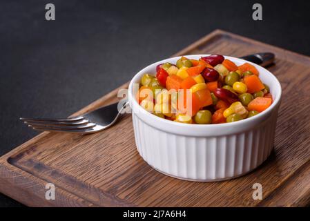 Eine Mischung aus gehacktem Gemüse, Paprika, Mais, Erbsen auf weißem Teller vor einem dunklen Betongrund Stockfoto