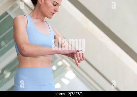 Sportliche Läuferin überprüft ihre intelligente Uhr, städtischen Hintergrund. Stockfoto